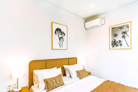 Cozy modern bedroom with rattan headboard bed, white linens, tropical palm and tree wall art, and wall-mounted AC unit.